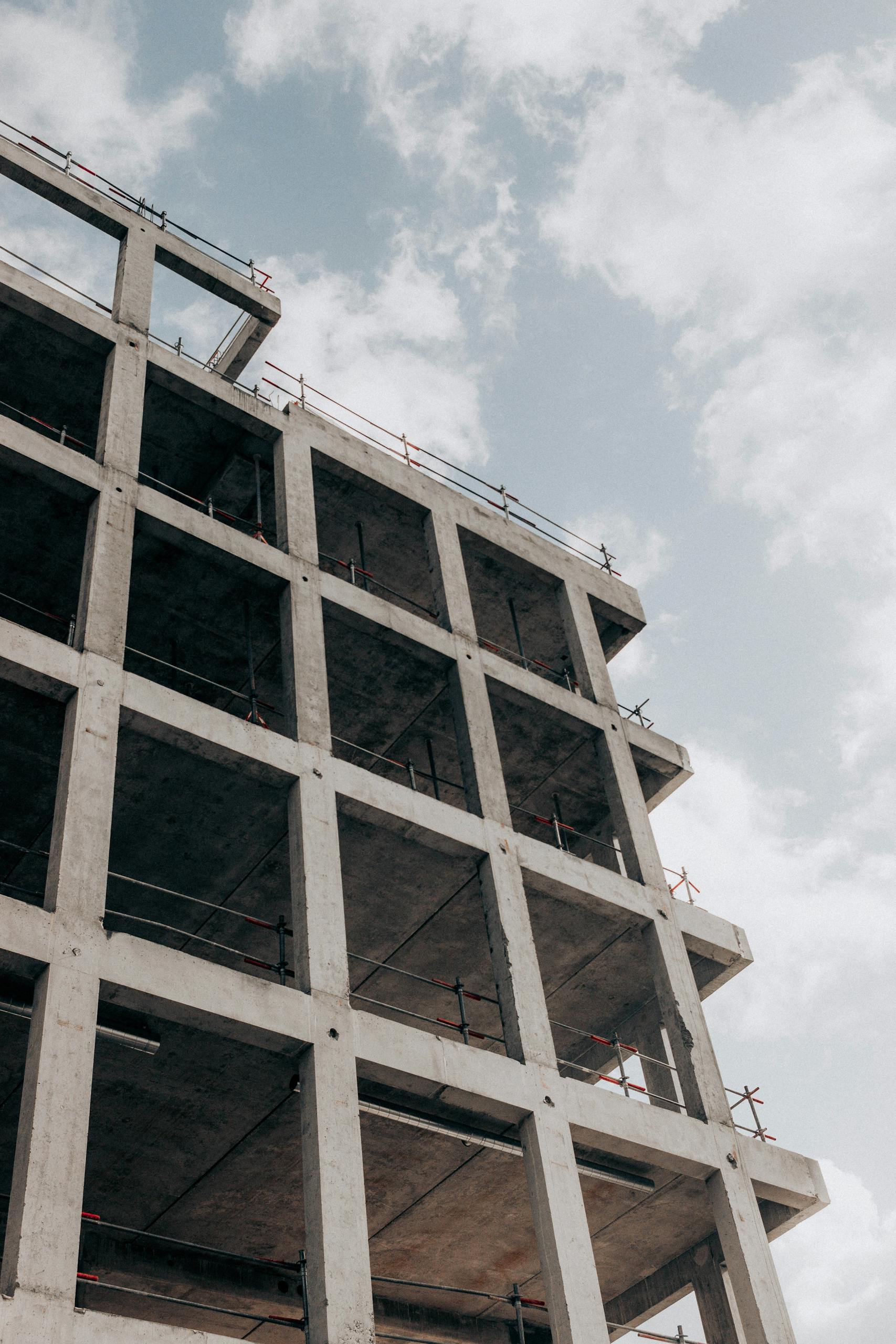 A modern multistory concrete building under construction, framed against a blue sky and clouds.