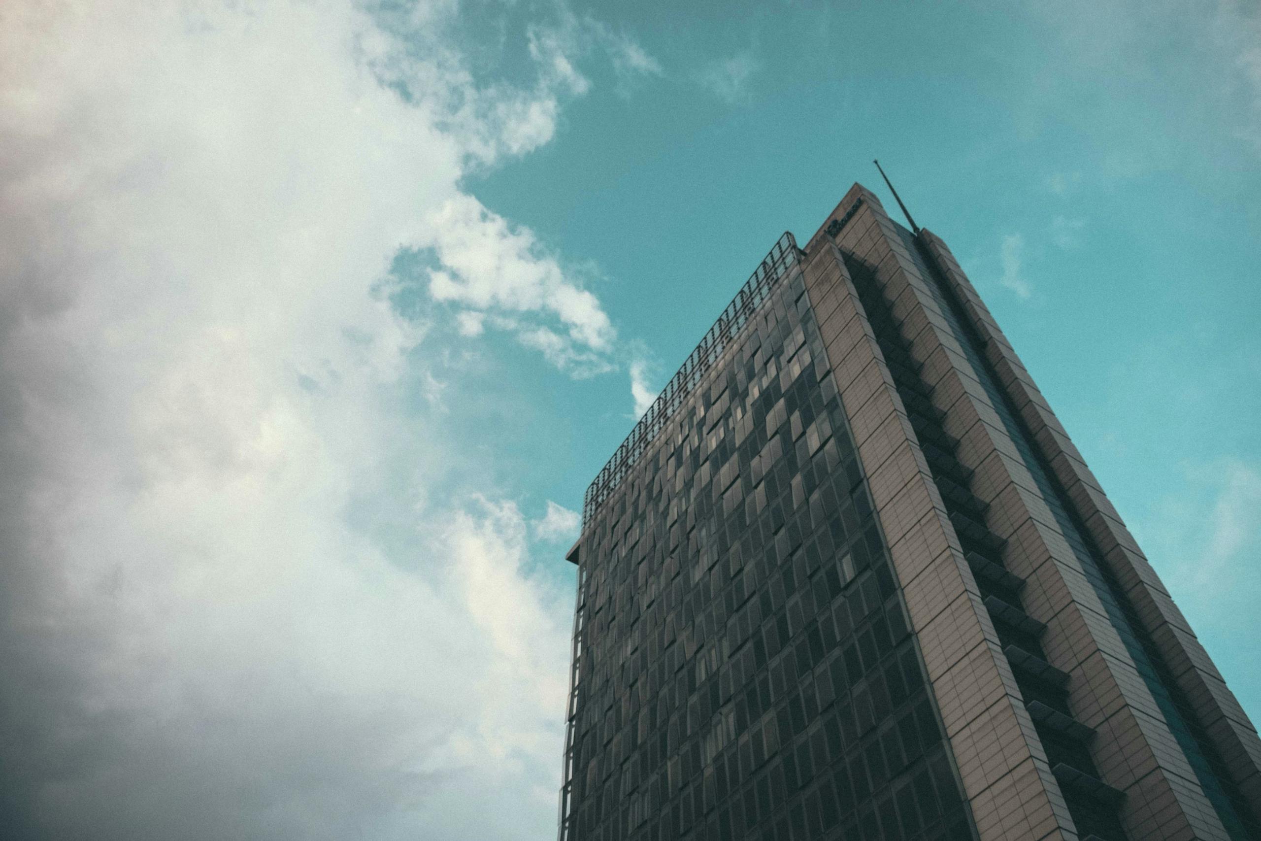 From below contemporary tall building with glass mirrored walls against cloudy blue sky